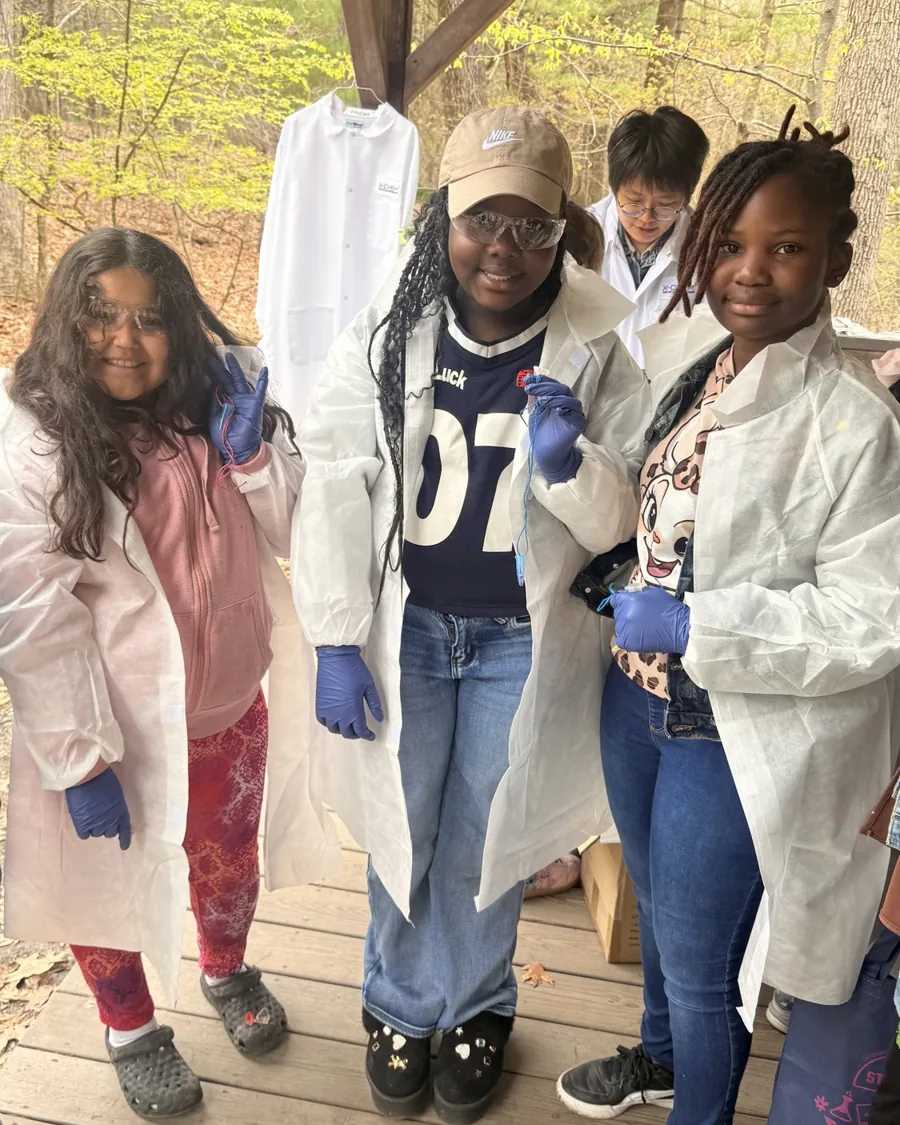 Three girls in lab coats and gloves during a hands-on STEM activity